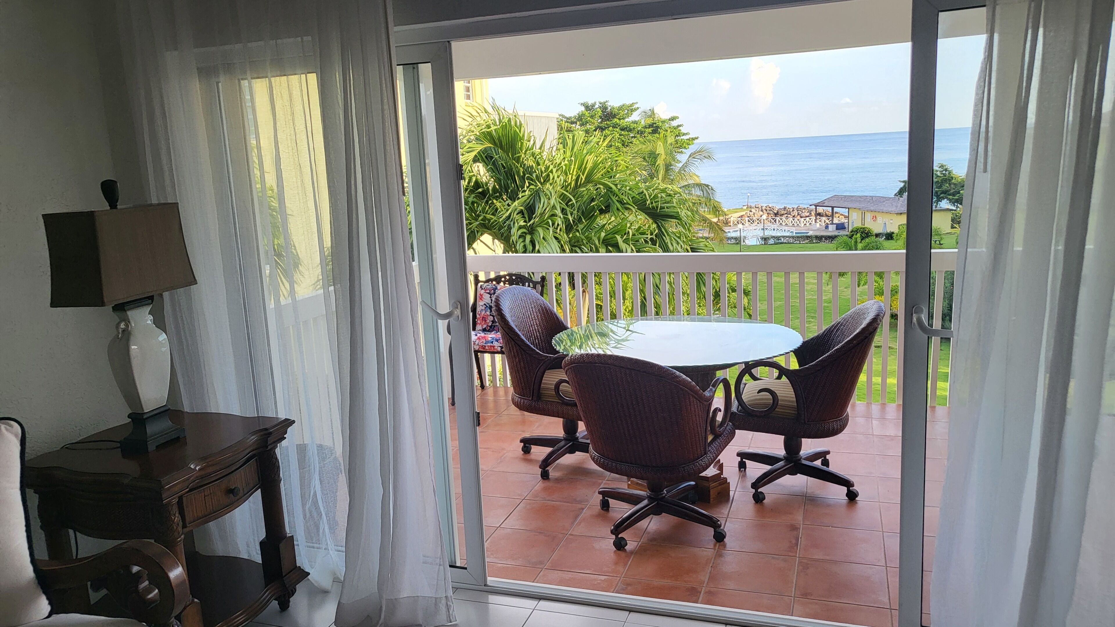 A room with a view of the sea, a table with chairs, and a lamp.
