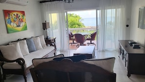 A living room with a sofa, a dining table, and chairs, a painting on the wall, and a view of the sea through a glass door. - Sea Palms Holidays (Tower Isle)