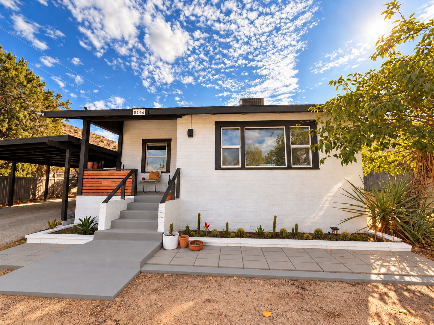 A modern two-story house with a covered patio, a small front garden, and a clear blue sky.