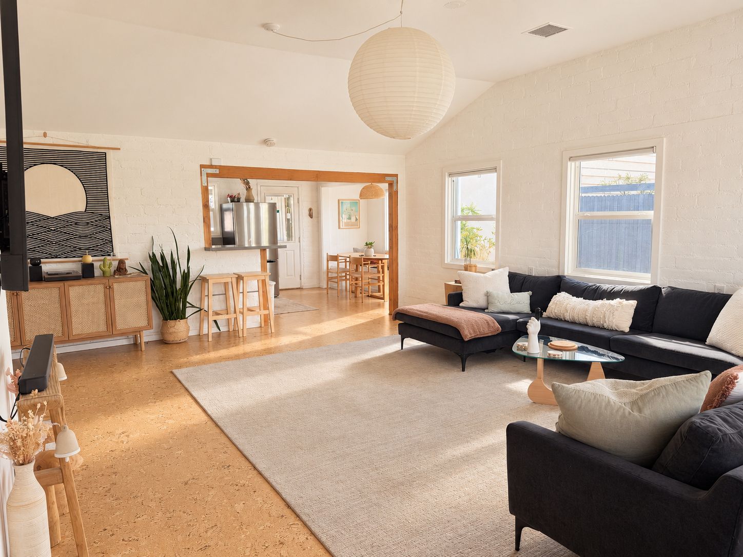 A spacious living room with a dark sofa, a coffee table, and a dining area with wooden furniture.