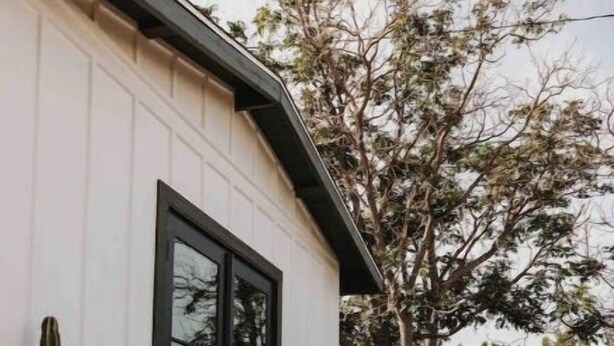 A white building with a black door, a wooden deck, and potted plants. - Joshua Tree - Under the Stars-Pool, Spa & Fire pit (Yucca Valley)
