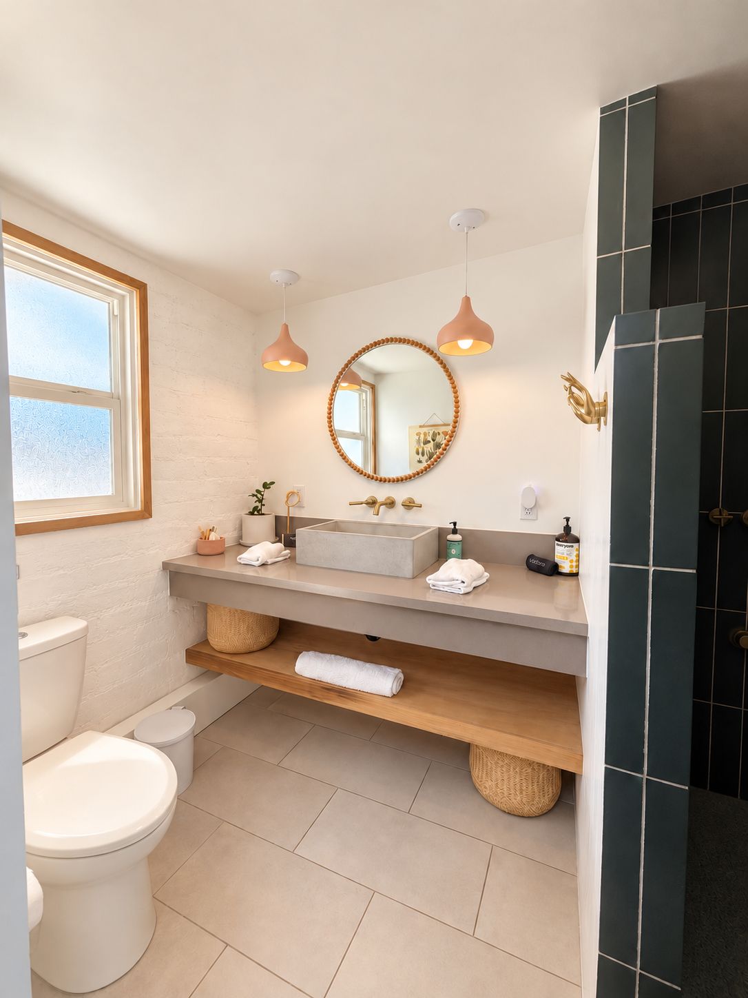 Une salle de bain moderne avec des toilettes blanches, un lavabo beige et un miroir au-dessus. On y trouve deux lampes suspendues, un porte-serviettes et un panier sur le comptoir.