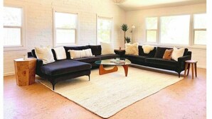 A modern living room with a sectional sofa, a coffee table, and a large window providing natural light. - Joshua Tree - Under the Stars-Pool, Spa & Fire pit (Yucca Valley)