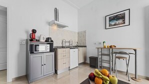 A modern kitchen with a microwave, kettle, and coffee maker on the counter, a small trash bin, and a table with fruits. - Home2Book Charming Apartment Teguise, Terrace (Nazaret)