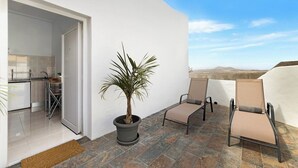 A modern outdoor patio with a potted palm tree, two lounge chairs, and a view of the desert landscape. - Home2Book Charming Apartment Teguise, Terrace (Nazaret)