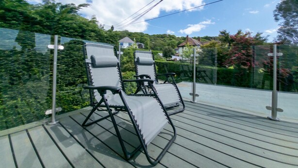 Una terraza con dos sillones reclinables y una barandilla de cristal.