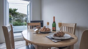 Una mesa de comedor con sillas, una botella de champán, copas y croissants.