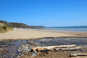 Ein Strand mit Kieselsteinen und Treibholz, ein klarer Himmel und ferne Hügel.