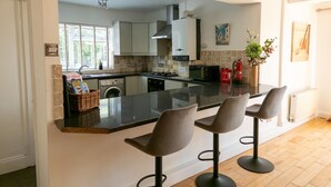A modern kitchen with a central island, bar stools, a washing machine, a stove, and a microwave.
