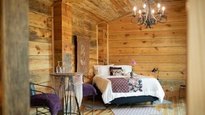 A cozy wooden cabin room with a bed, a small table, and a chair.