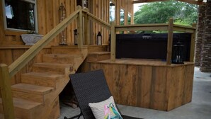 A wooden deck with a black lounge chair and a cushion, a staircase, and a covered barbecue area.