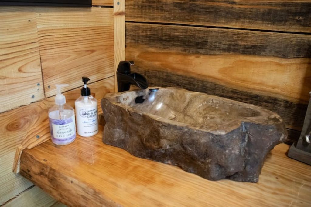 A rustic wooden bench with a stone sink and hand soap bottles.