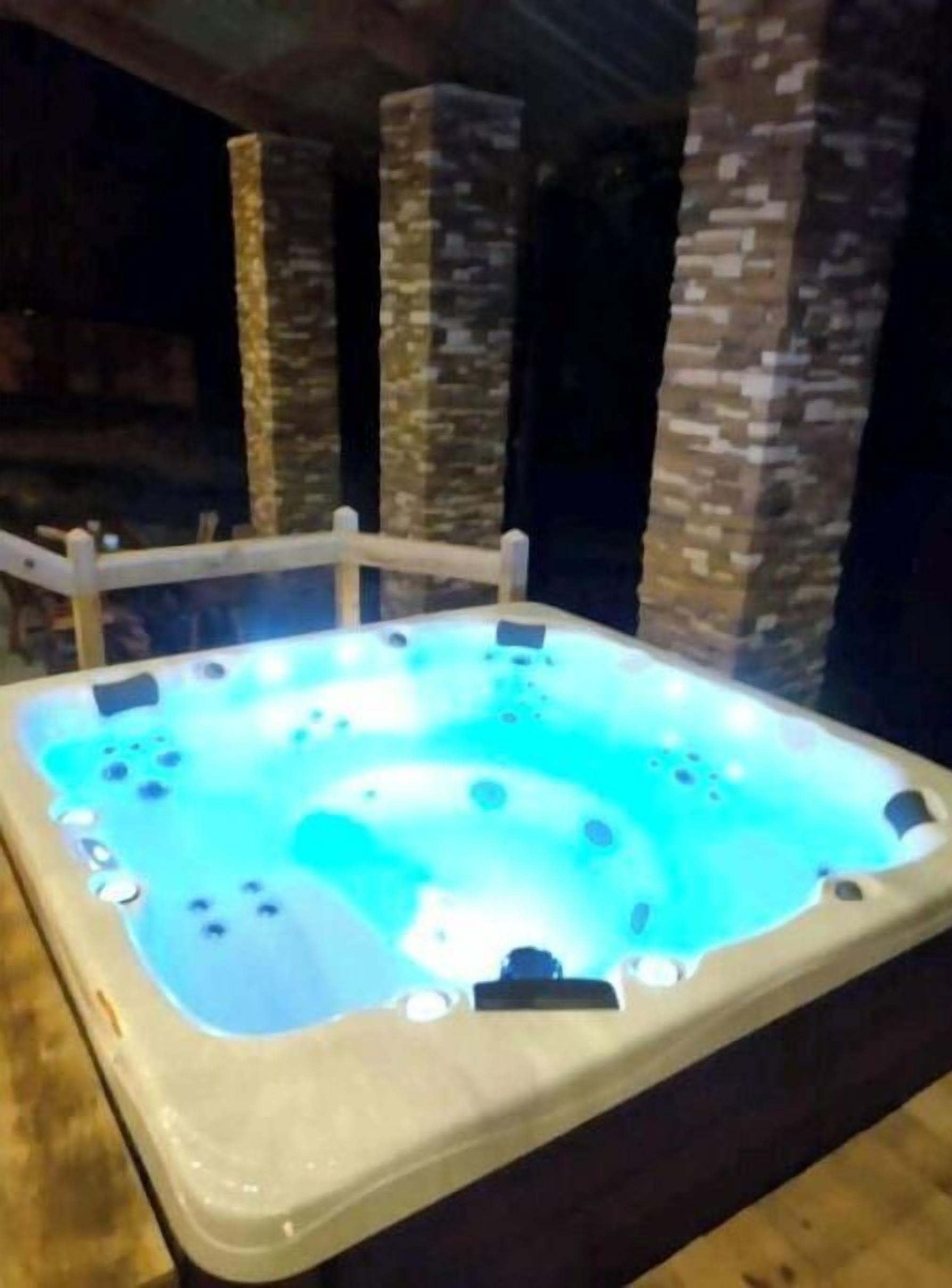 Una vasca idromassaggio con interni blu chiaro, circondata da pilastri in pietra e un pontile in legno.