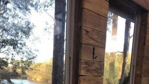 Eine Hütte mit großen Fenstern mit Blick auf einen See, ein Teleskop auf einem Stativ und mehrere Kerzen auf einem Fensterbrett.