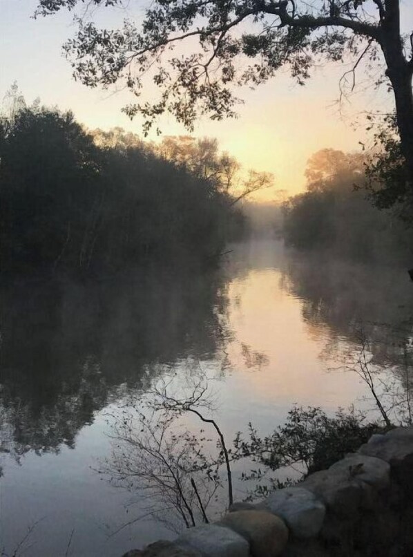 Une rivière paisible, bordée d’arbres des deux côtés, et entourée d’un mur de pierres.