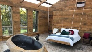 Eine Hütte mit einer großen Steinbadewanne, einem Hängeschlafzimmer und großen Fenstern.