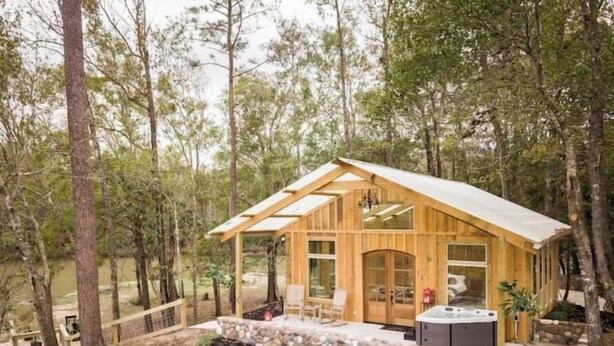 Eine Holzhütte mit Steinunterbau, großen Fenstern und einem Whirlpool.