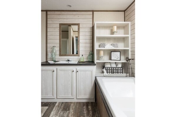 A modern bathroom with a wooden vanity, a large mirror, and a white bathtub.