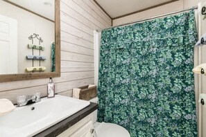 A bathroom with a white sink, wooden vanity, and a shower curtain with a floral pattern.