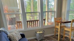 Una sala de estar con un sofá azul, una silla de madera y ventanas amplias con vistas al exterior.