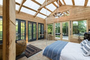 A spacious bedroom with a large bed, a stone accent piece, and a view of the outdoors through large windows. - Secluded Romantic Cabin on the Water (Lumberton)
