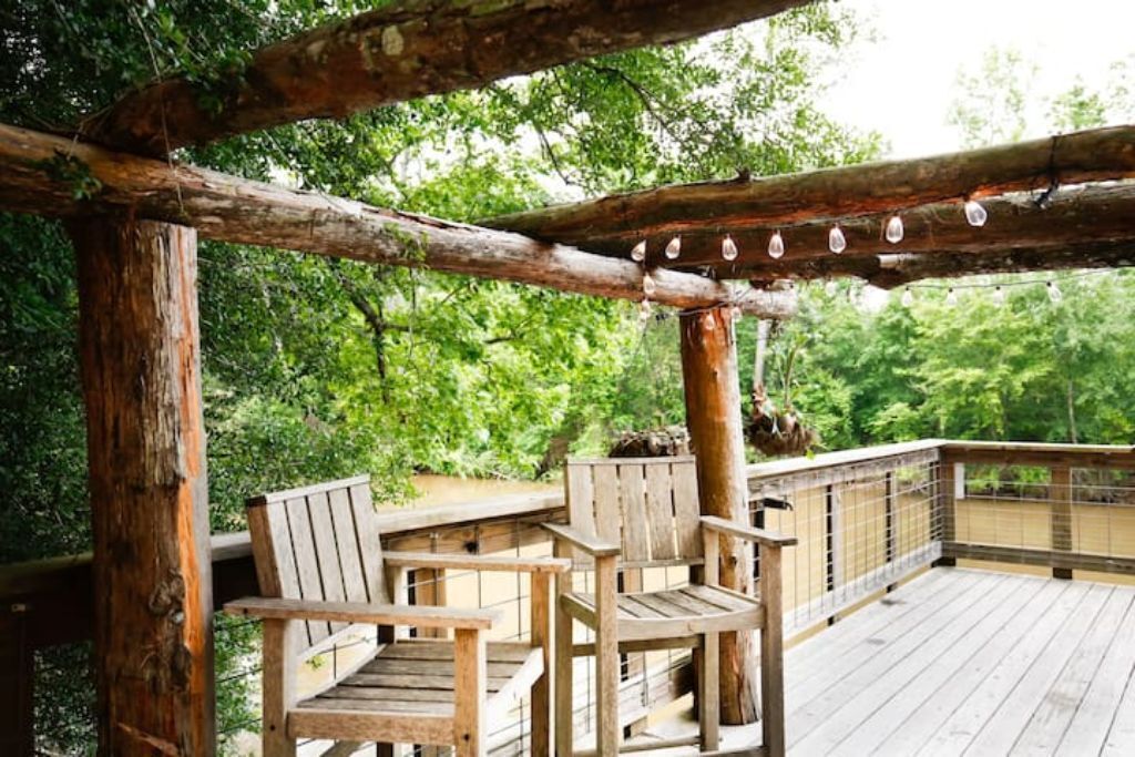 A wooden deck with two chairs and a railing, surrounded by greenery.