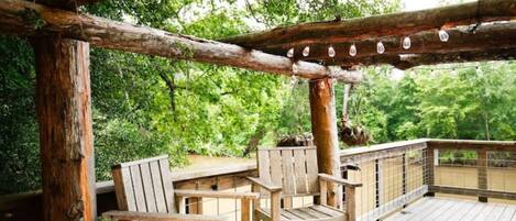 A wooden deck with two chairs and a railing, surrounded by greenery.