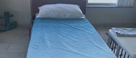 Een bed met een blauw-witte deken, een wit kussen en uitzicht op een waterlichaam door een raam.