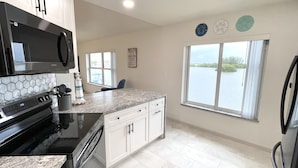 A kitchen with a large island, a microwave, a stove, and a refrigerator. There is a window with a view of a body of water.