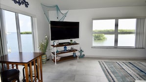 A living room with a large window, a flat-screen TV, a wooden table, and a blue-striped rug.