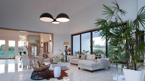 A spacious living room with a modern sofa, a wicker chair, and a large potted plant. - Casa de Campo’s Ultimate Group Villa Pool, Cinema & Pickleball (La Romana)