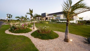 A modern house with a well-maintained lawn, palm trees, and flower beds. - Casa de Campo’s Ultimate Group Villa Pool, Cinema & Pickleball (La Romana)