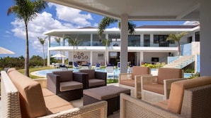A modern resort with outdoor seating, a pool, and a large building with multiple balconies. - Casa de Campo’s Ultimate Group Villa Pool, Cinema & Pickleball (La Romana)