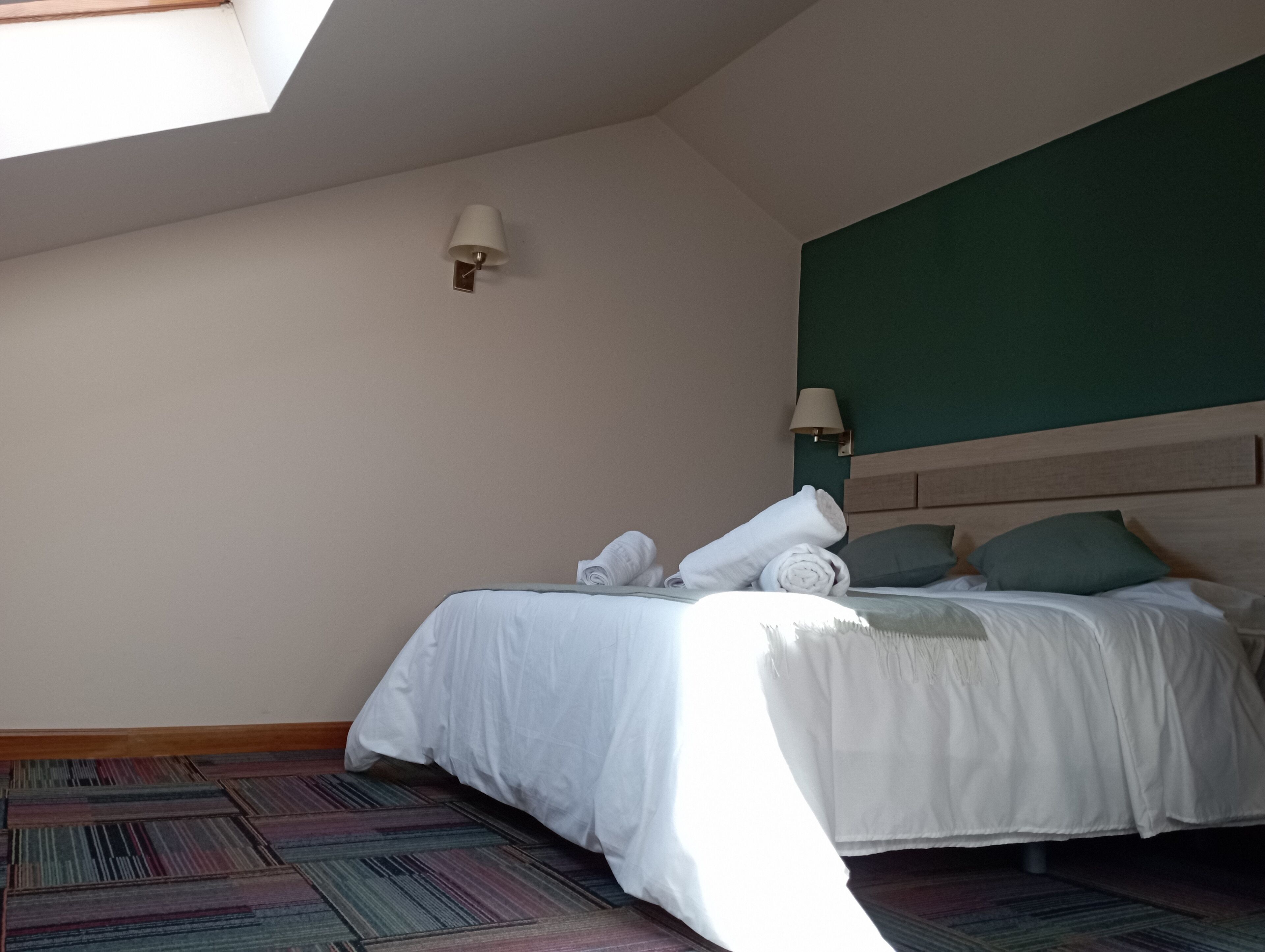 A hotel room with a bed, a nightstand, a lamp, and a view of the sky through a skylight.