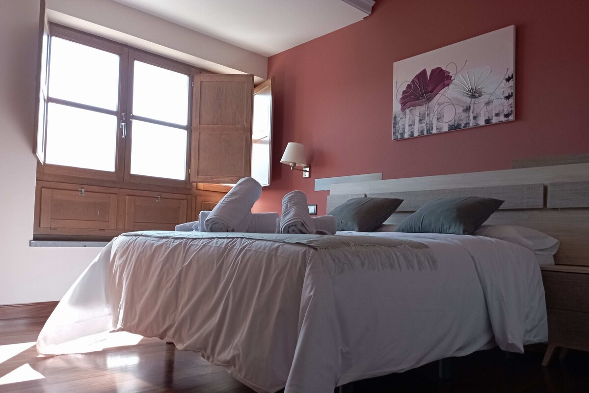 A bedroom with a bed, pillows, a nightstand, a lamp, and a window with wooden shutters.