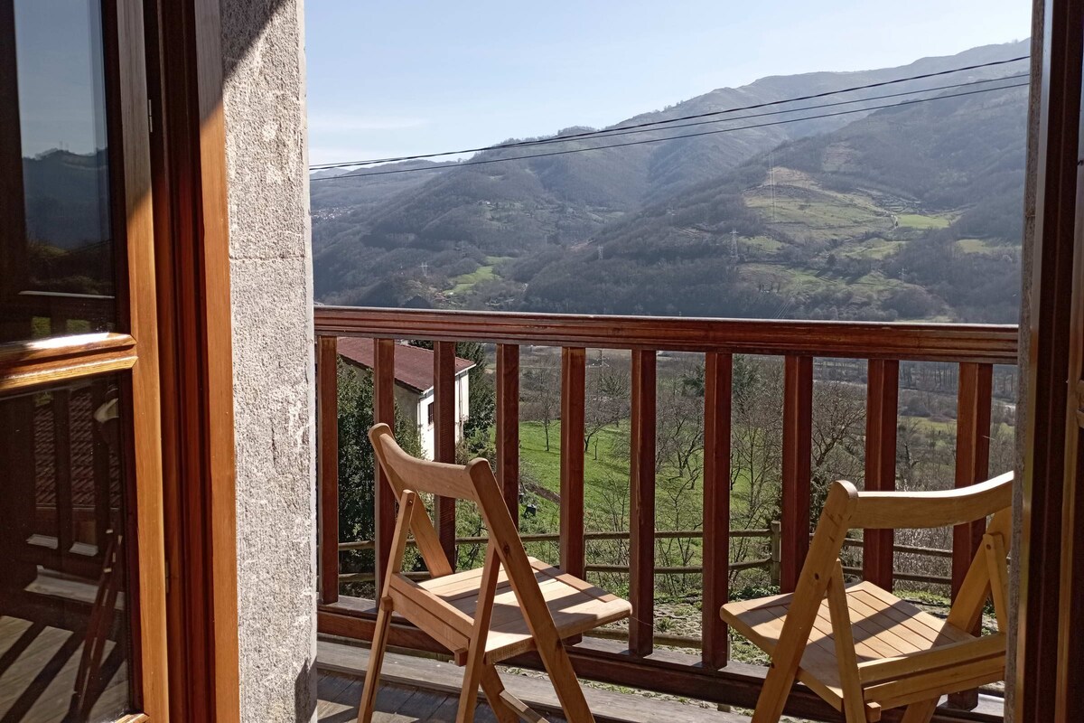 A balcony with two wooden chairs overlooking a mountainous landscape.