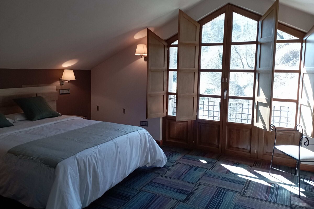 A bedroom with a large bed, two wall-mounted lamps, a window with wooden shutters, and a patterned floor.