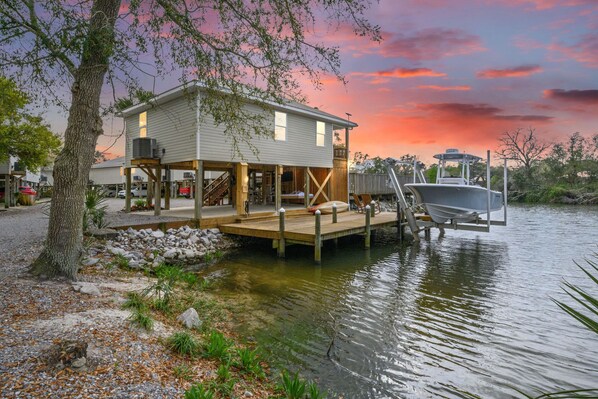 A house with a deck extending over water, a dock, and a boat.