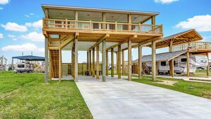 Estructura de madera de dos pisos con un balcón, un patio cubierto y un camino de hormigón.
