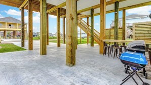 Un espacio al aire libre techado con vigas de madera y suelo de concreto, que incluye una parrilla y asientos.