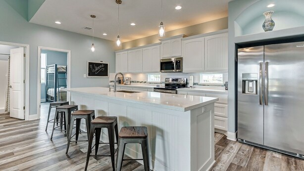 Una cocina moderna con armarios blancos, electrodomésticos de acero inoxidable y una isla central con taburetes de bar.