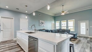 Una cocina amplia con una isla grande, armarios blancos e iluminación colgante.