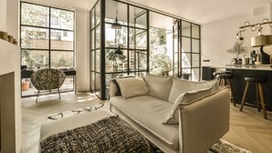 Una sala de estar moderna con un sofá, un sillón estampado y una zona de cocina con taburetes.
