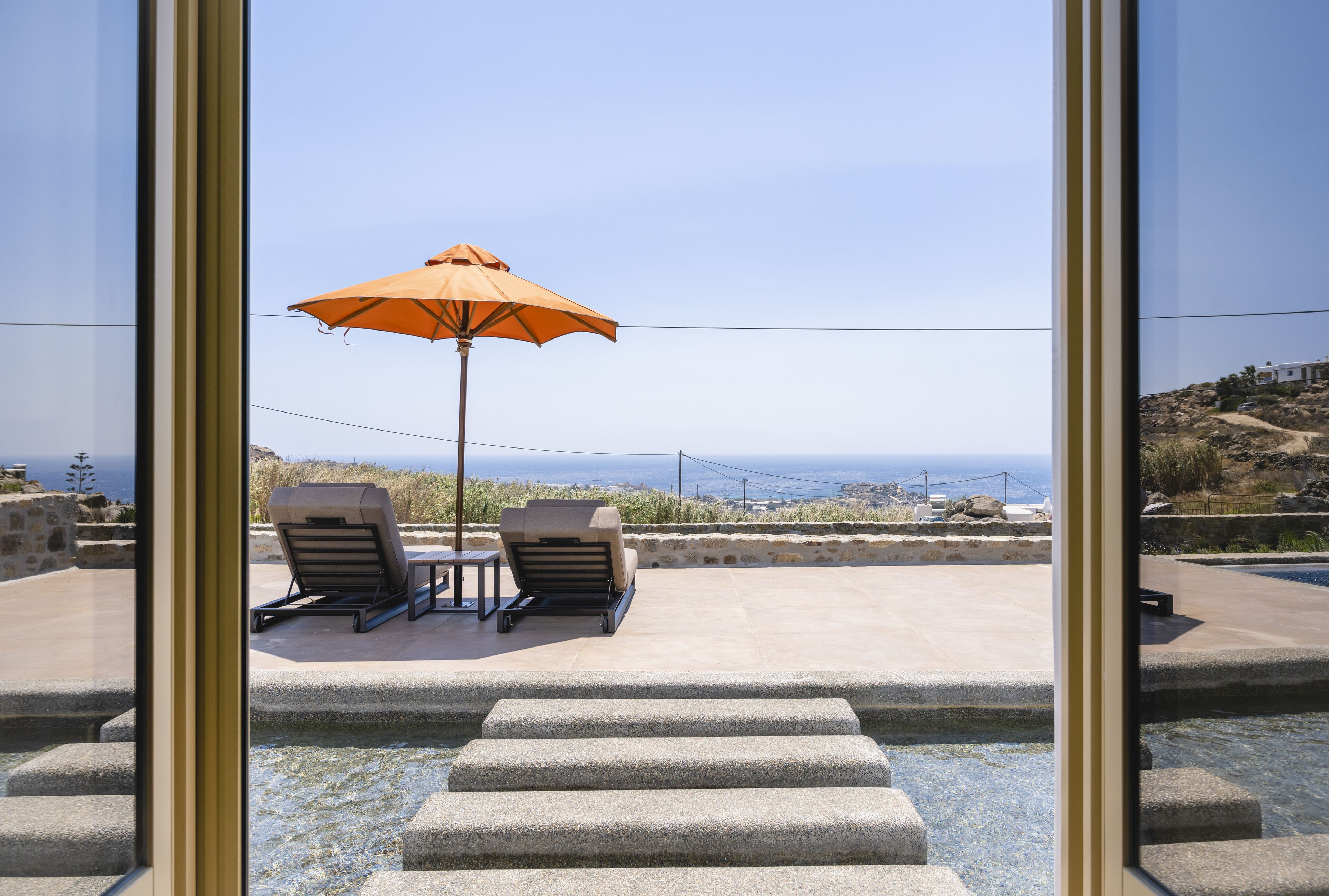 A patio with two lounge chairs and an orange umbrella, overlooking a scenic view.