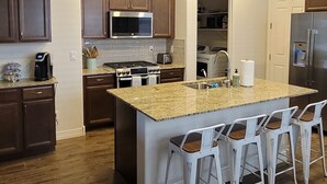 Une cuisine moderne avec des meubles en bois, un plan de travail en granit et un îlot central doté de tabourets de bar.
