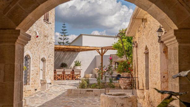 Une cour extérieure avec des murs en pierre, une pergola en bois et des plantes en pot.