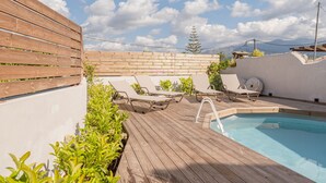 Un espace piscine aménagé sur le toit, avec une terrasse en bois, des chaises longues et une piscine.