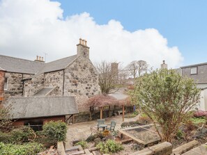 A stone building with a thatched roof, a stone staircase, and a garden area with a wooden table and chairs. - 20 South High Street (Banff)