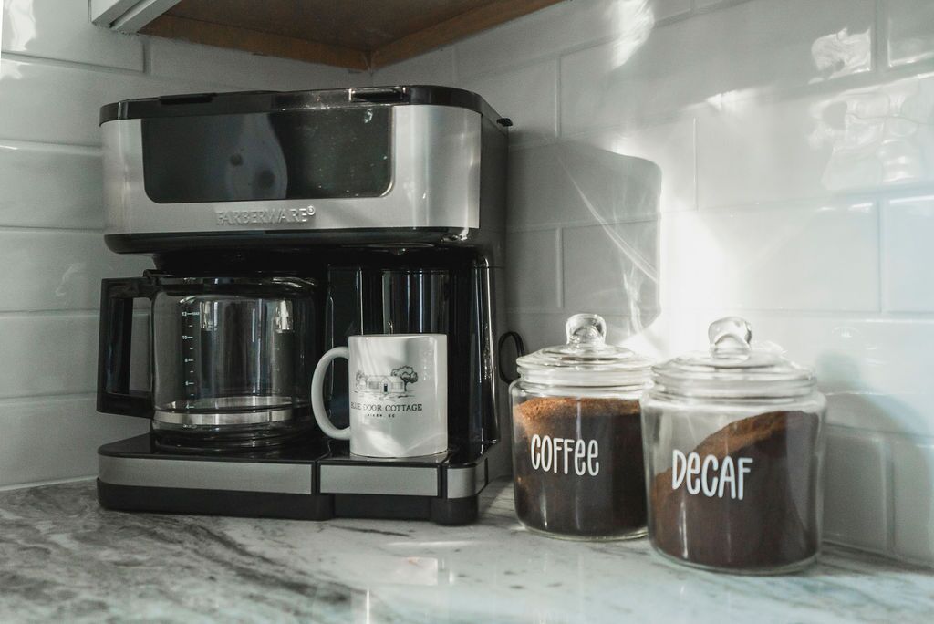 Eine Kaffeemaschine mit zwei Glasbehältern, beschriftet mit 'Kaffee' und 'Entkoffeiniert', auf einer Marmorarbeitsplatte.