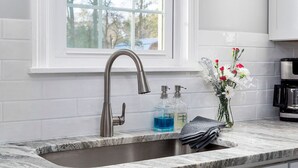 A kitchen with a white countertop, a stainless steel sink, a window above the sink, and a coffee maker on the right.